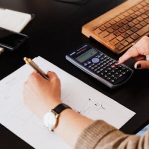 Close-up of hands working with a calculator and notebook on a desk, analyzing documents.