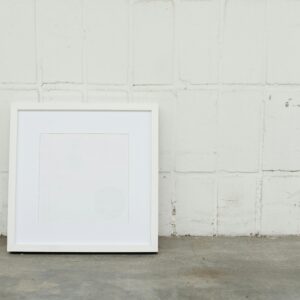 A minimalist white picture frame against a textured concrete wall, offering ample copy space.